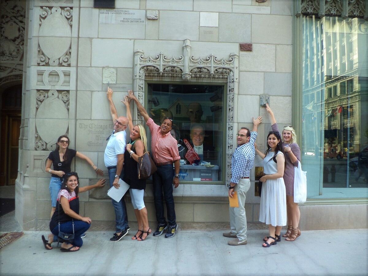 Scavenger Hunt team posing in front of a building pointing to different features on the stone