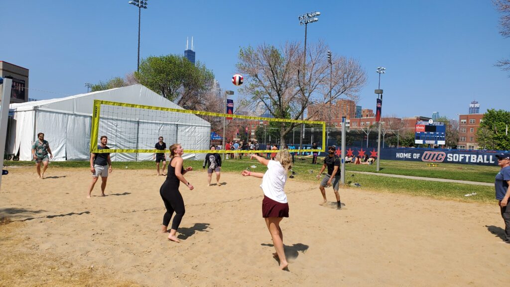 UIC Picnic Grounds - Guests playing volleyball at the sand volleyball courts with Chicago skyline in the background and a large tent